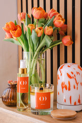 Decorative items including a vase of orange tulips, a bottle, a candle, and a diffuser on a wooden surface.