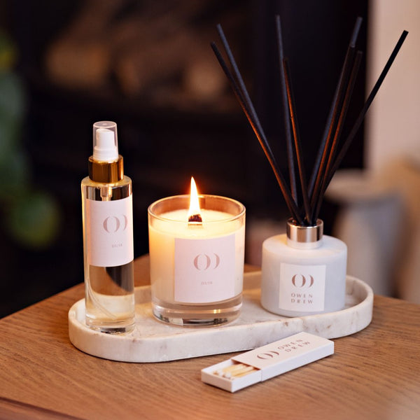 Candle, diffuser, and spray bottle on a tray with a blurred background
