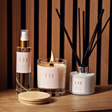 Candle, diffuser, and bottle on a wooden surface with striped background