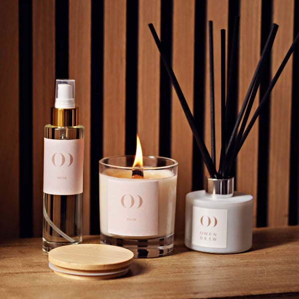 Candle, diffuser, and bottle on a wooden surface with striped background