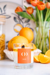 Candle with an orange label in a setting with oranges and flowers